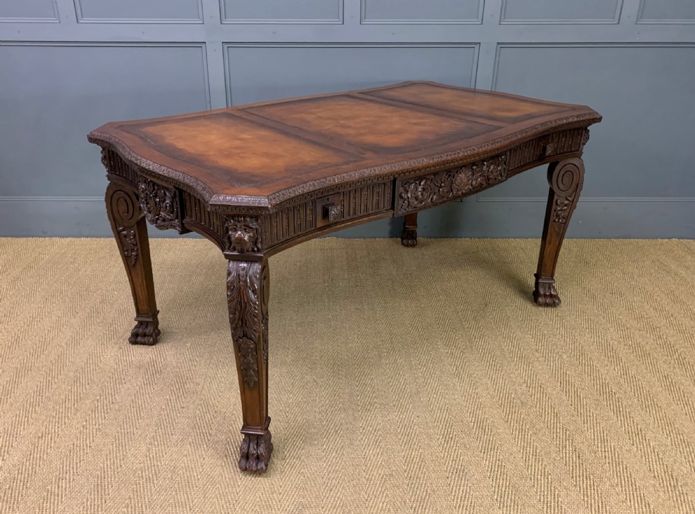 A carved mahogany writing table with a three-section inset leather top, detailed frieze carvings, and carved legs with claw feet.