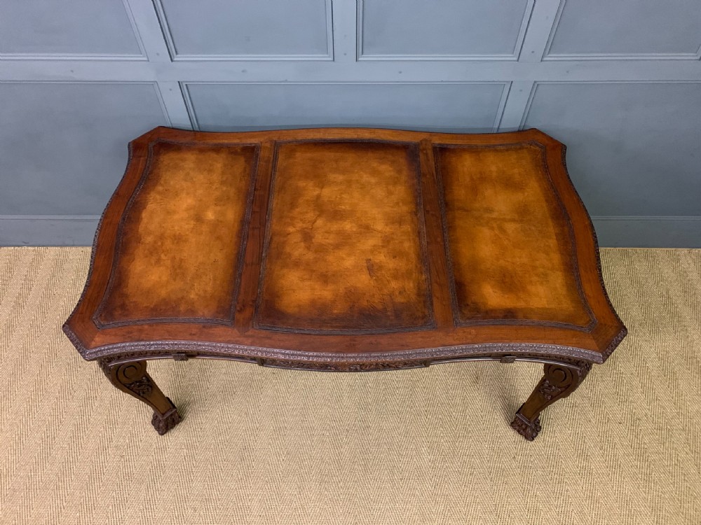 A carved mahogany writing table with a three-section inset leather top, detailed frieze carvings, and carved legs with claw feet. View IV