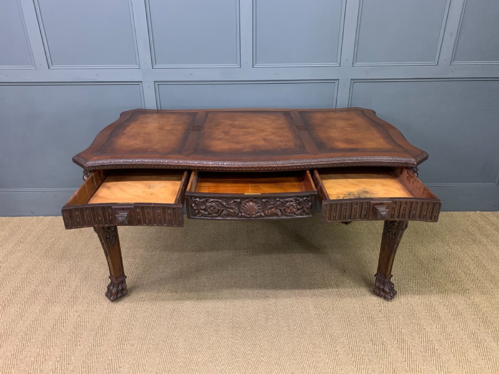 A carved mahogany writing table with a three-section inset leather top, detailed frieze carvings, and carved legs with claw feet. View X