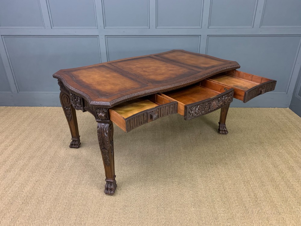 A carved mahogany writing table with a three-section inset leather top, detailed frieze carvings, and carved legs with claw feet. View XVII