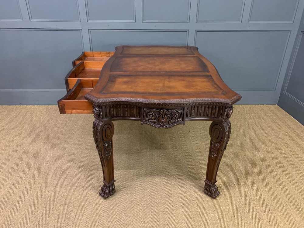 A carved mahogany writing table with a three-section inset leather top, detailed frieze carvings, and carved legs with claw feet. View XIX