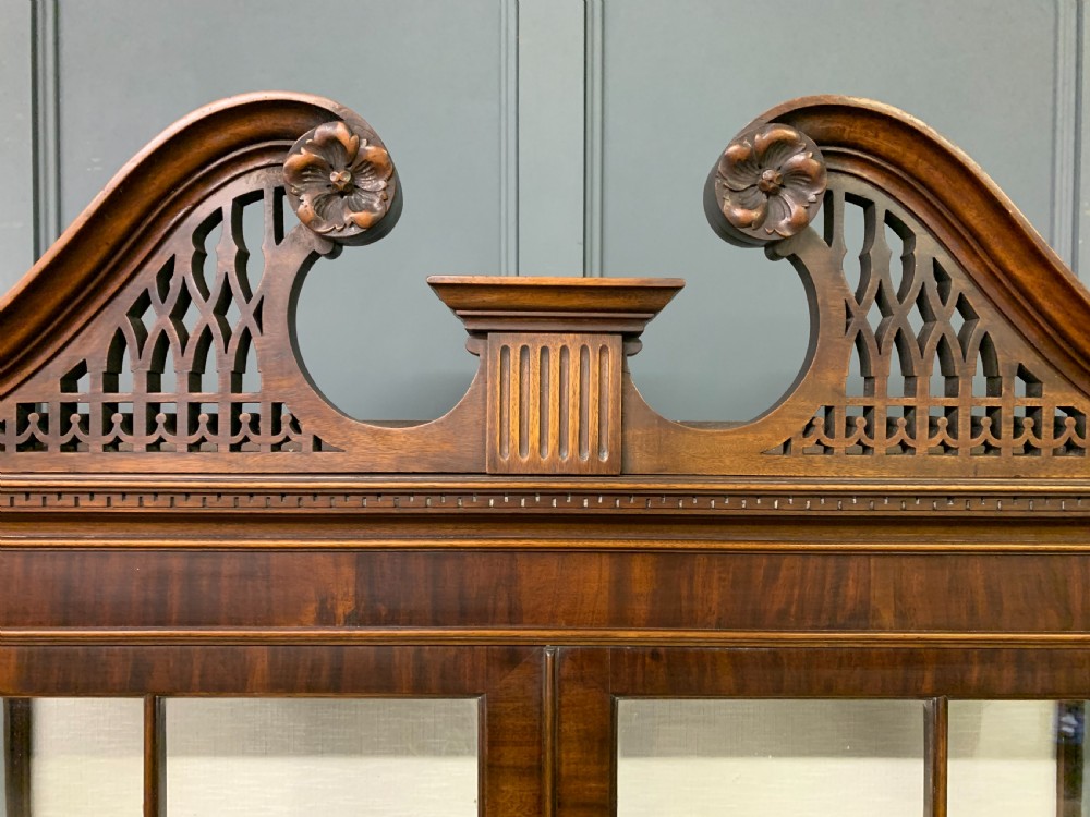 A Chippendale style mahogany display cabinet featuring a swan-neck pediment, glazed twin doors, internal glass shelves, and carved feet. View IV