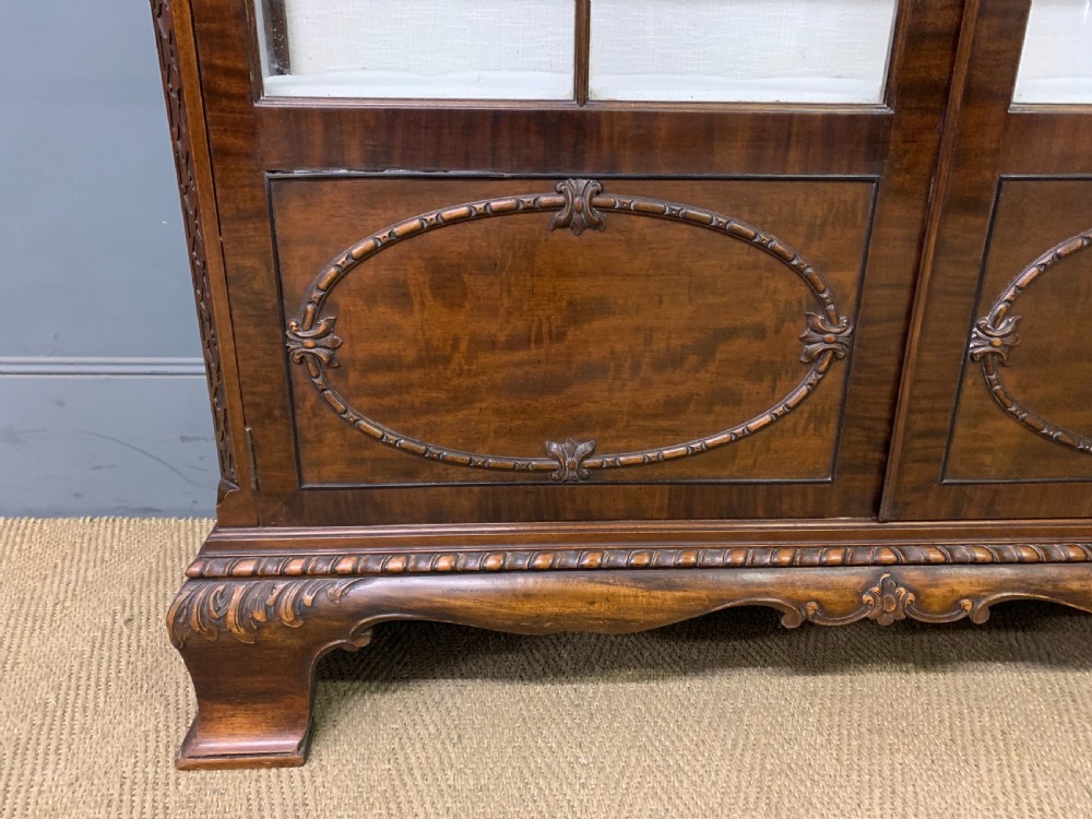 A Chippendale style mahogany display cabinet featuring a swan-neck pediment, glazed twin doors, internal glass shelves, and carved feet. View V