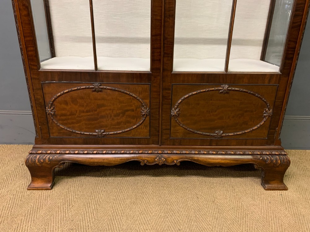 A Chippendale style mahogany display cabinet featuring a swan-neck pediment, glazed twin doors, internal glass shelves, and carved feet. View VI
