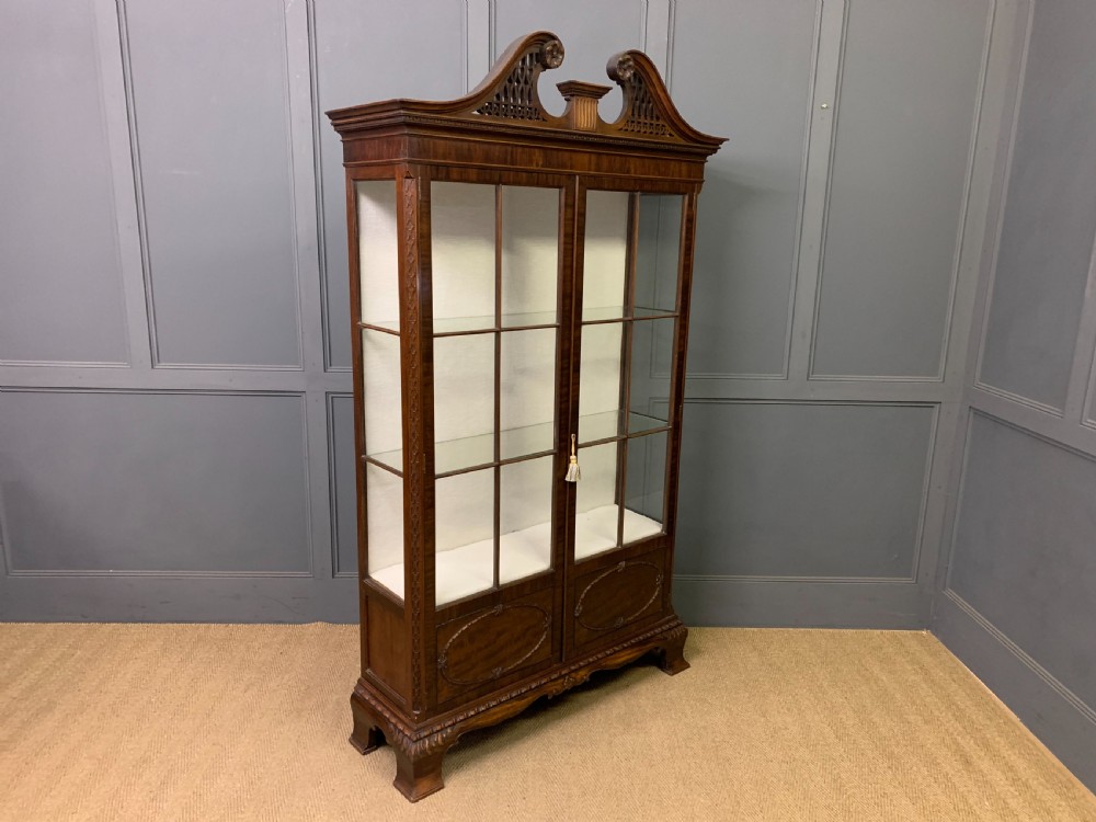 A Chippendale style mahogany display cabinet featuring a swan-neck pediment, glazed twin doors, internal glass shelves, and carved feet. View VII
