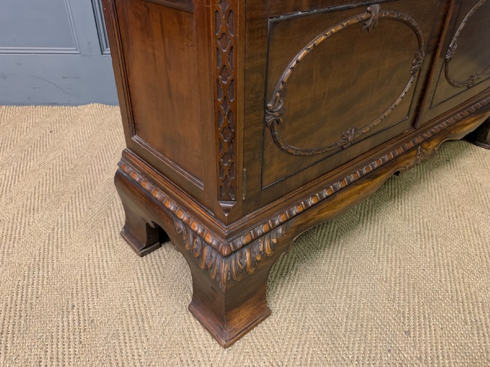 A Chippendale style mahogany display cabinet featuring a swan-neck pediment, glazed twin doors, internal glass shelves, and carved feet. View IX