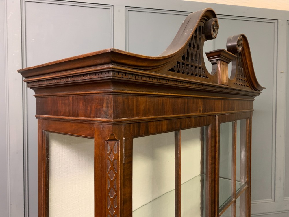 A Chippendale style mahogany display cabinet featuring a swan-neck pediment, glazed twin doors, internal glass shelves, and carved feet. View X