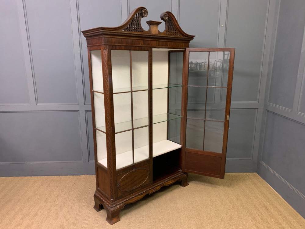 A Chippendale style mahogany display cabinet featuring a swan-neck pediment, glazed twin doors, internal glass shelves, and carved feet. View XI
