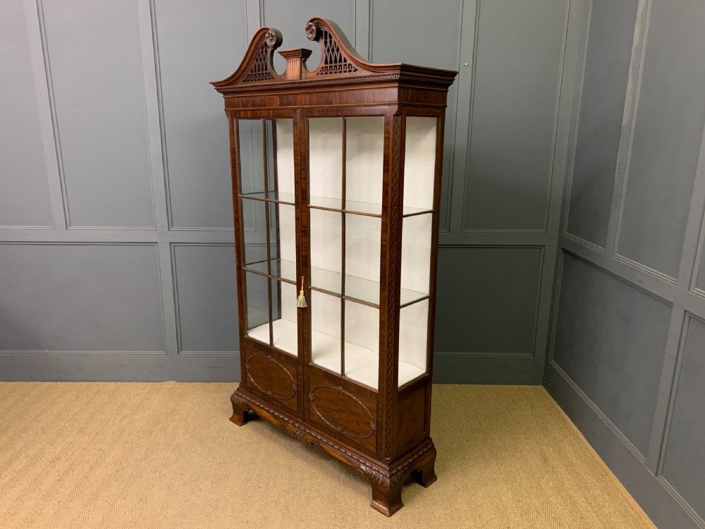 A Chippendale style mahogany display cabinet featuring a swan-neck pediment, glazed twin doors, internal glass shelves, and carved feet. View XII