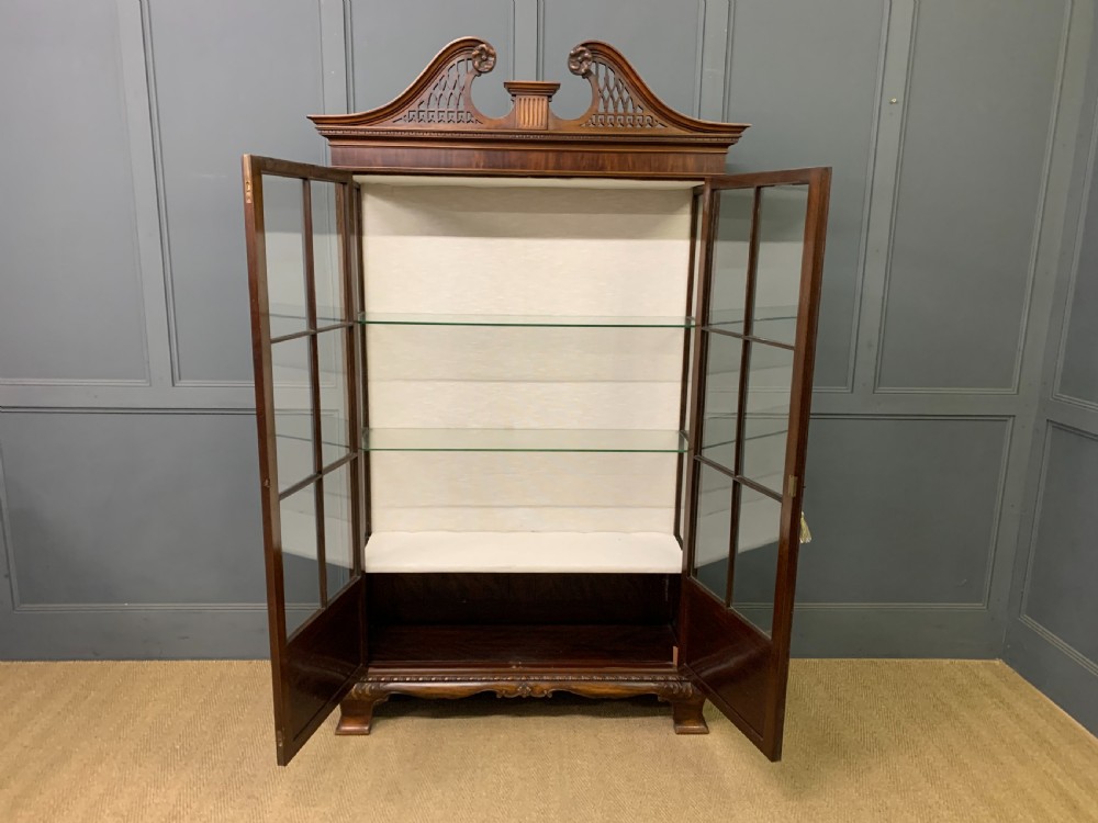A Chippendale style mahogany display cabinet featuring a swan-neck pediment, glazed twin doors, internal glass shelves, and carved feet. View XIII