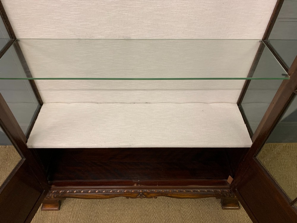 A Chippendale style mahogany display cabinet featuring a swan-neck pediment, glazed twin doors, internal glass shelves, and carved feet. View XIV