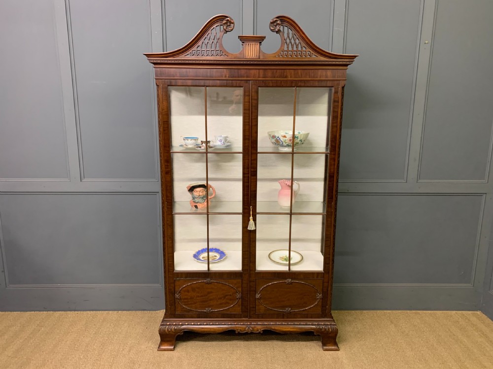 A Chippendale style mahogany display cabinet featuring a swan-neck pediment, glazed twin doors, internal glass shelves, and carved feet. View XV