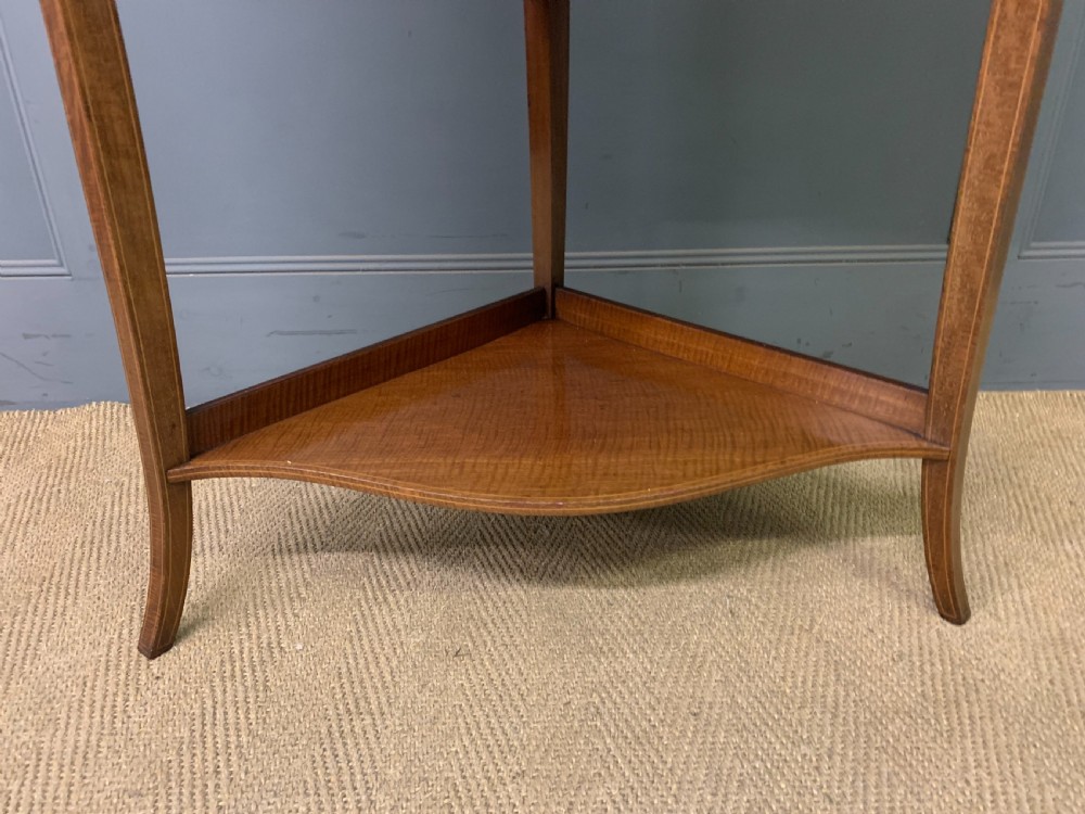 An Edwardian inlaid mahogany corner display cabinet featuring a swan-neck pediment, a glass door with a green fabric lining, neoclassical urn marquetry on the lower doors, and slender legs with an undertier. View V