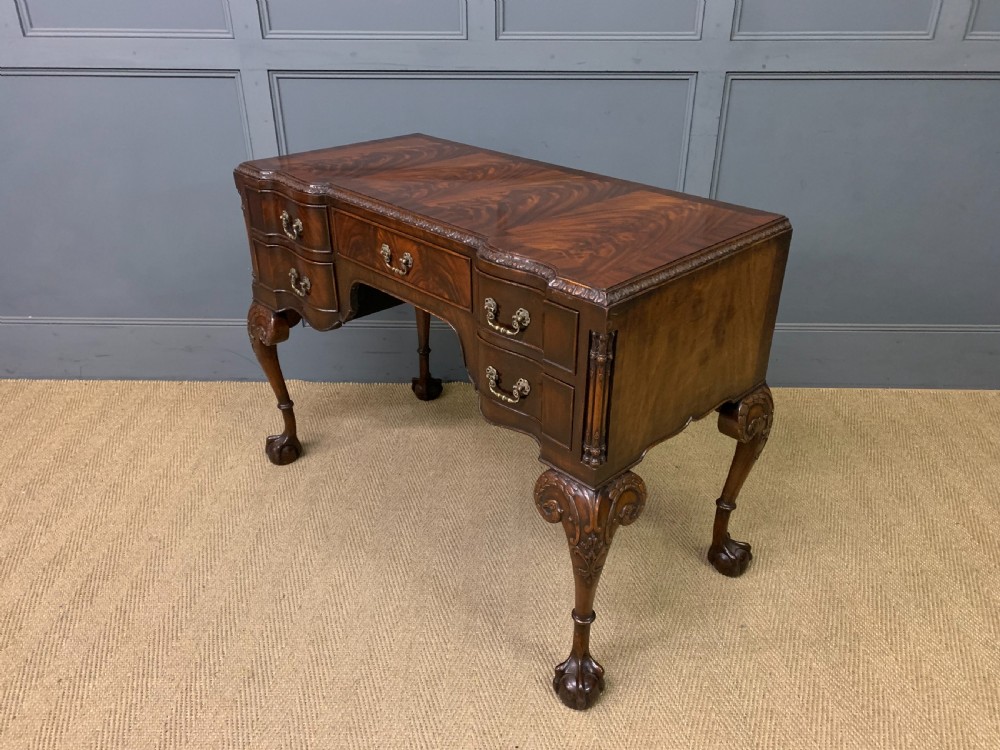 A flame mahogany Chippendale style writing desk featuring a shaped top, five brass-handled drawers, and carved cabriole legs with ball and claw feet.
