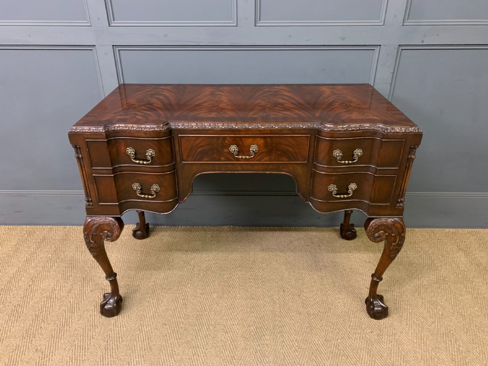 A flame mahogany Chippendale style writing desk featuring a shaped top, five brass-handled drawers, and carved cabriole legs with ball and claw feet. View II