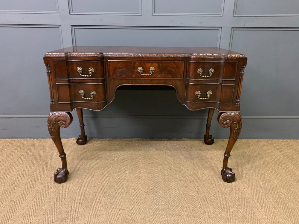 A flame mahogany Chippendale style writing desk featuring a shaped top, five brass-handled drawers, and carved cabriole legs with ball and claw feet. View III