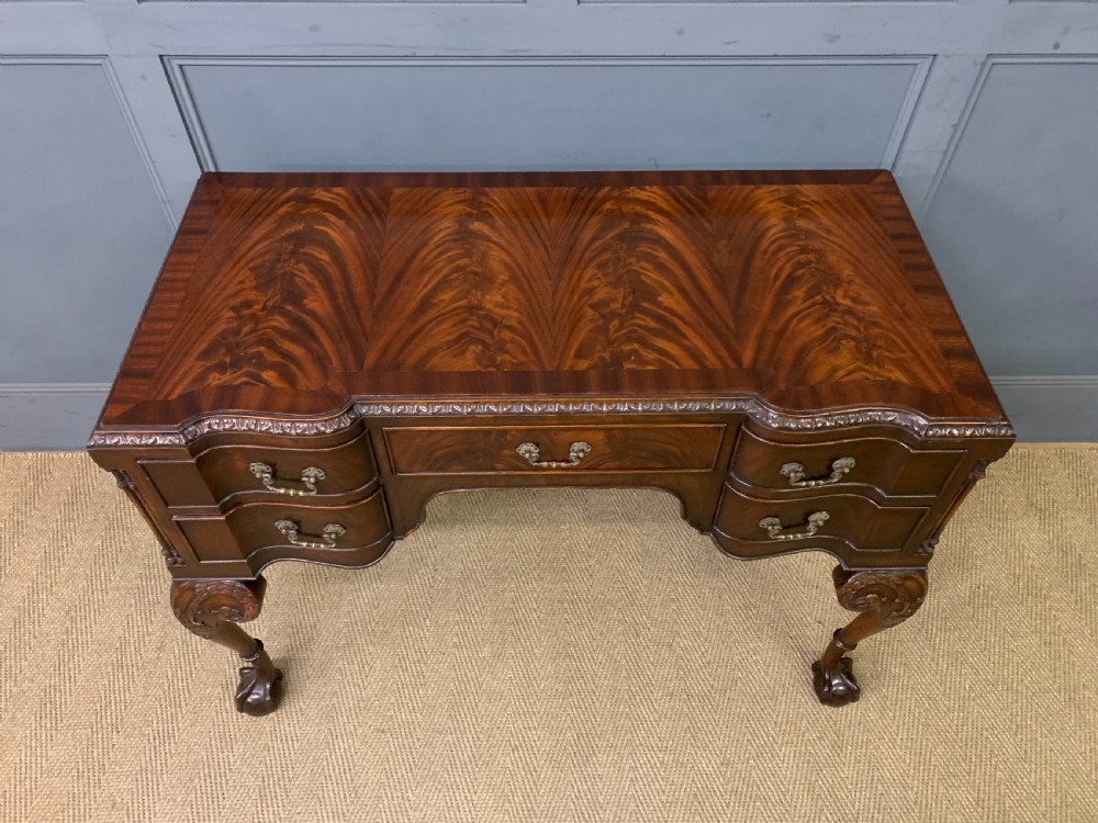 A flame mahogany Chippendale style writing desk featuring a shaped top, five brass-handled drawers, and carved cabriole legs with ball and claw feet. View IV