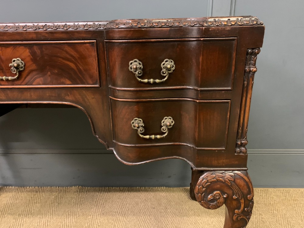 A flame mahogany Chippendale style writing desk featuring a shaped top, five brass-handled drawers, and carved cabriole legs with ball and claw feet. View V