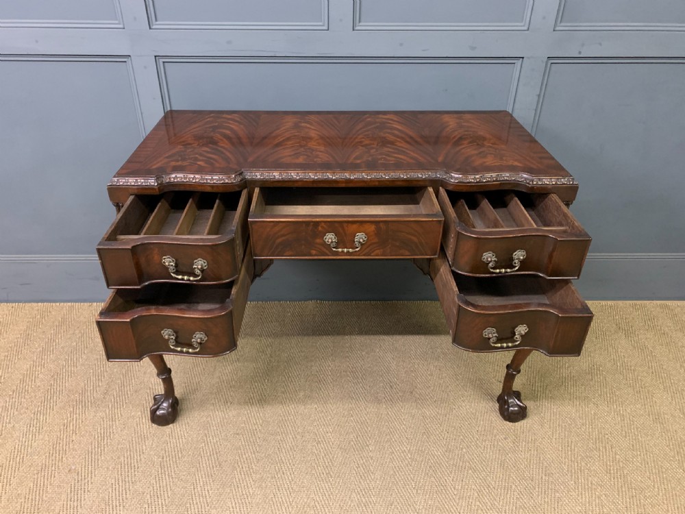 A flame mahogany Chippendale style writing desk featuring a shaped top, five brass-handled drawers, and carved cabriole legs with ball and claw feet. View VII