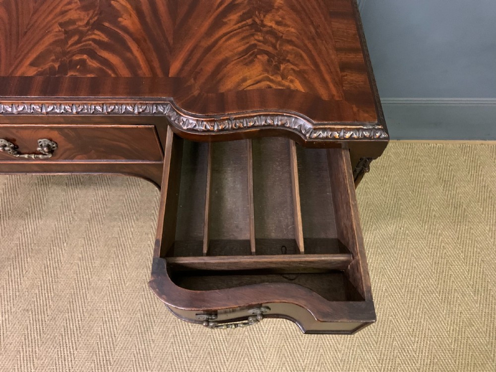 A flame mahogany Chippendale style writing desk featuring a shaped top, five brass-handled drawers, and carved cabriole legs with ball and claw feet. View VIII