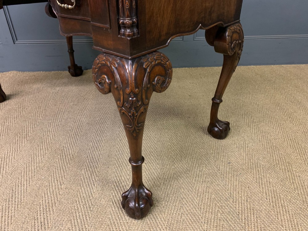 A flame mahogany Chippendale style writing desk featuring a shaped top, five brass-handled drawers, and carved cabriole legs with ball and claw feet. View X
