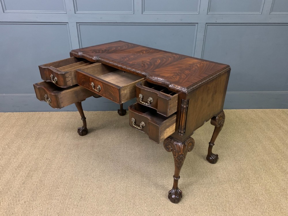 A flame mahogany Chippendale style writing desk featuring a shaped top, five brass-handled drawers, and carved cabriole legs with ball and claw feet. View XI