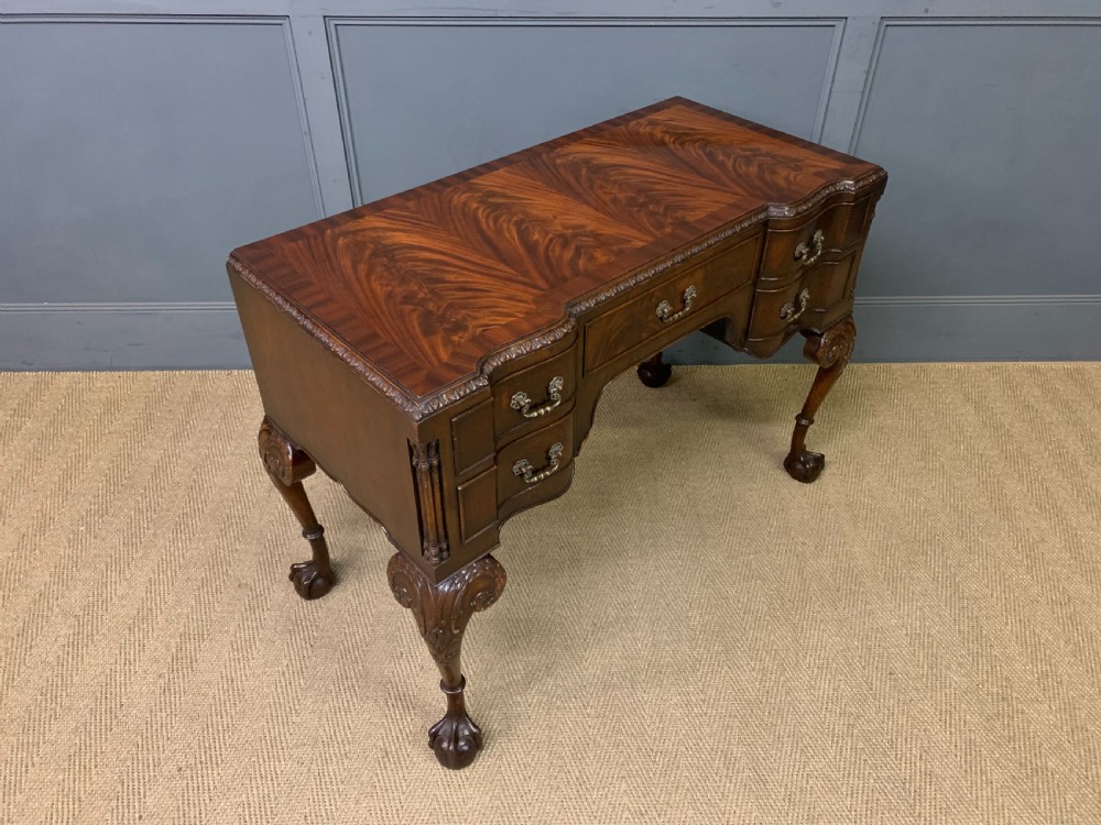 A flame mahogany Chippendale style writing desk featuring a shaped top, five brass-handled drawers, and carved cabriole legs with ball and claw feet. View XII