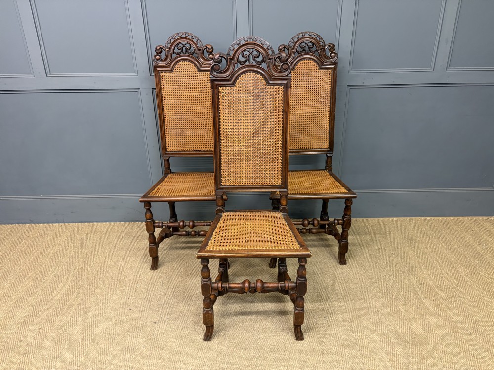 A set of three dark timber Carolean style side chairs featuring high arched carved cresting, woven cane backrest panels, cane seats, and turned stretchers. View II