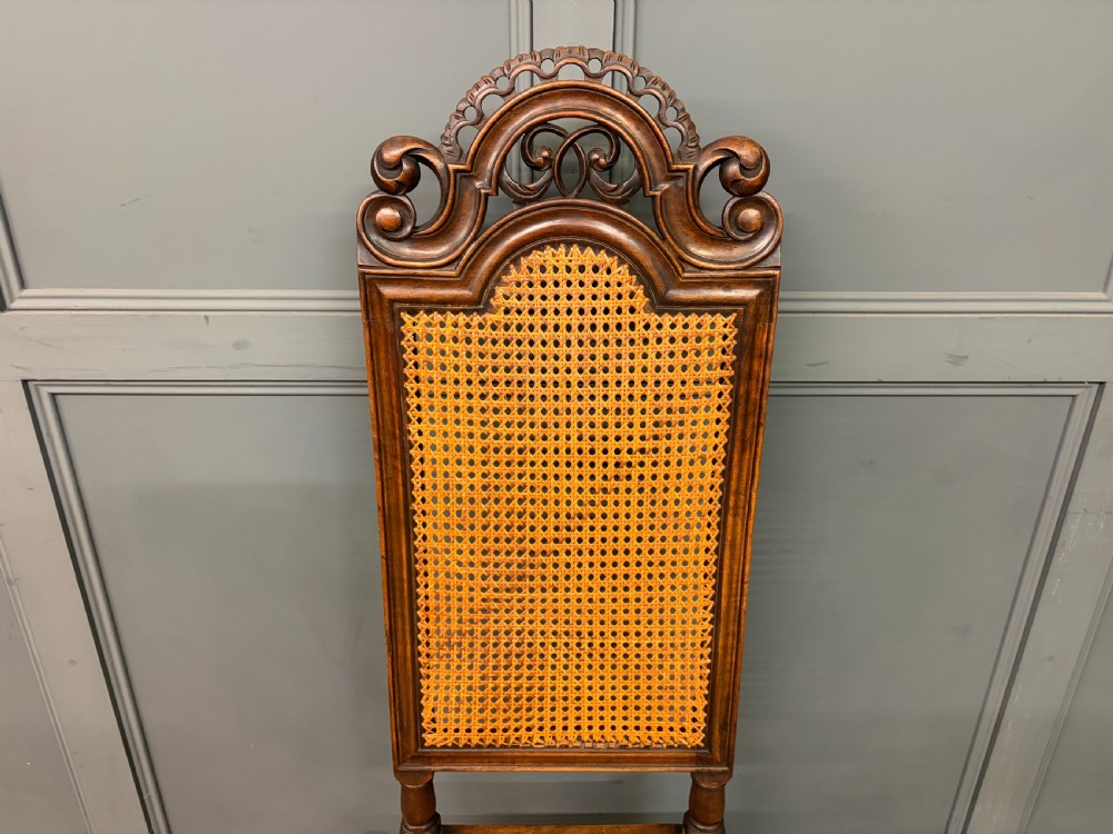A set of three dark timber Carolean style side chairs featuring high arched carved cresting, woven cane backrest panels, cane seats, and turned stretchers. View III