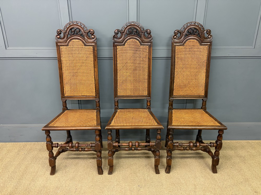 A set of three dark timber Carolean style side chairs featuring high arched carved cresting, woven cane backrest panels, cane seats, and turned stretchers. View IV