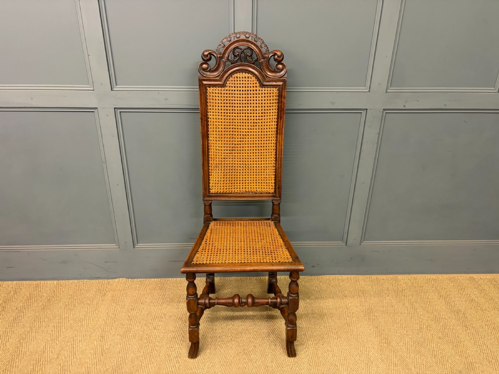 A set of three dark timber Carolean style side chairs featuring high arched carved cresting, woven cane backrest panels, cane seats, and turned stretchers. View V
