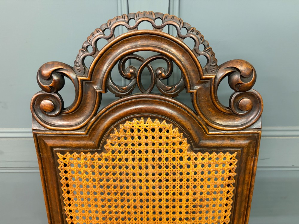 A set of three dark timber Carolean style side chairs featuring high arched carved cresting, woven cane backrest panels, cane seats, and turned stretchers. View VI