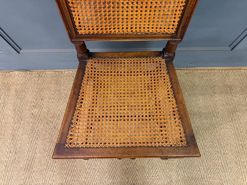 A set of three dark timber Carolean style side chairs featuring high arched carved cresting, woven cane backrest panels, cane seats, and turned stretchers. View VII