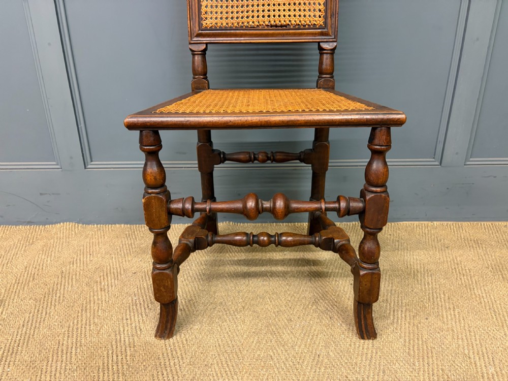 A set of three dark timber Carolean style side chairs featuring high arched carved cresting, woven cane backrest panels, cane seats, and turned stretchers. View VIII