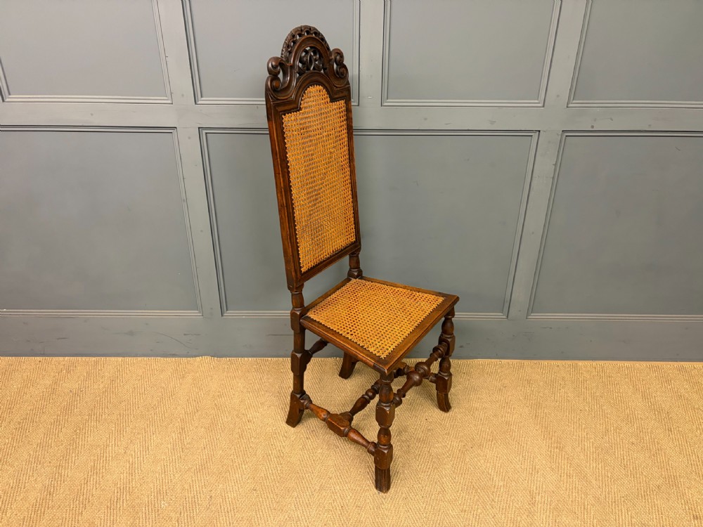 A set of three dark timber Carolean style side chairs featuring high arched carved cresting, woven cane backrest panels, cane seats, and turned stretchers. View IX