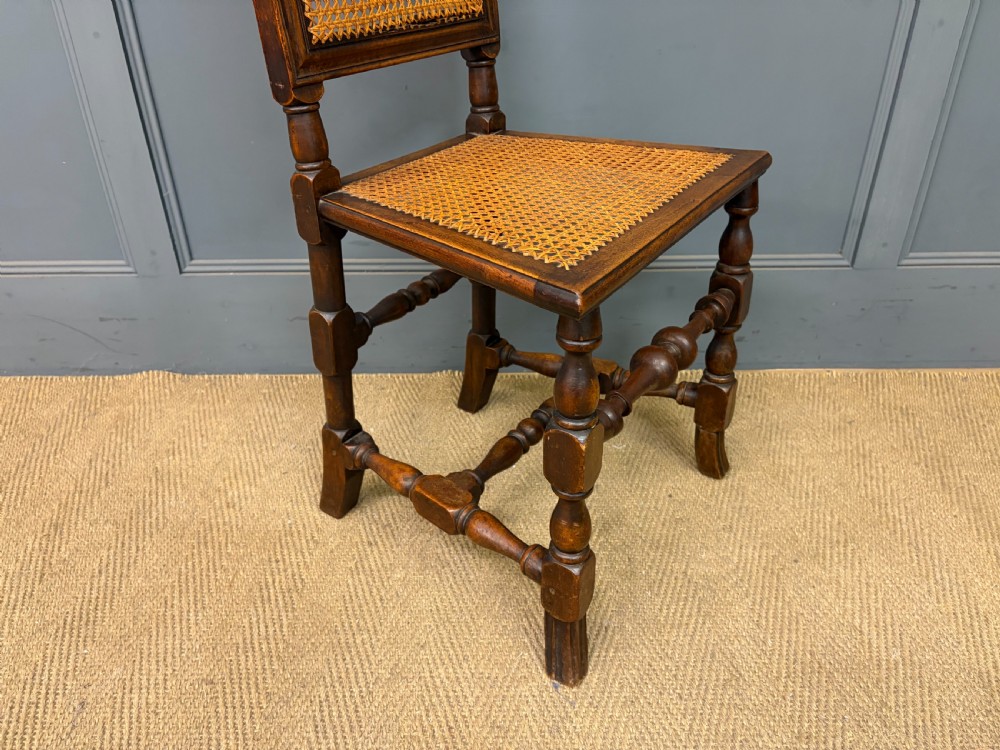 A set of three dark timber Carolean style side chairs featuring high arched carved cresting, woven cane backrest panels, cane seats, and turned stretchers. View X