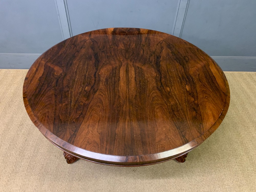 A William IV rosewood tilt-top loo table featuring a richly figured oval top mounted on a turned pedestal and a tri-form base with carved feet. View V