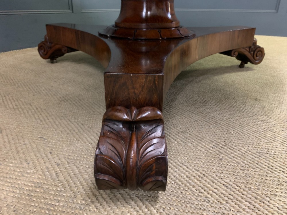 A William IV rosewood tilt-top loo table featuring a richly figured oval top mounted on a turned pedestal and a tri-form base with carved feet. View IX