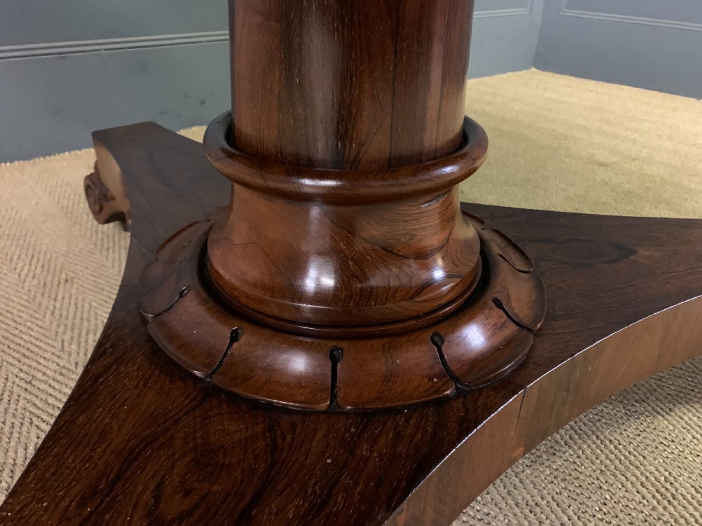 A William IV rosewood tilt-top loo table featuring a richly figured oval top mounted on a turned pedestal and a tri-form base with carved feet. View X