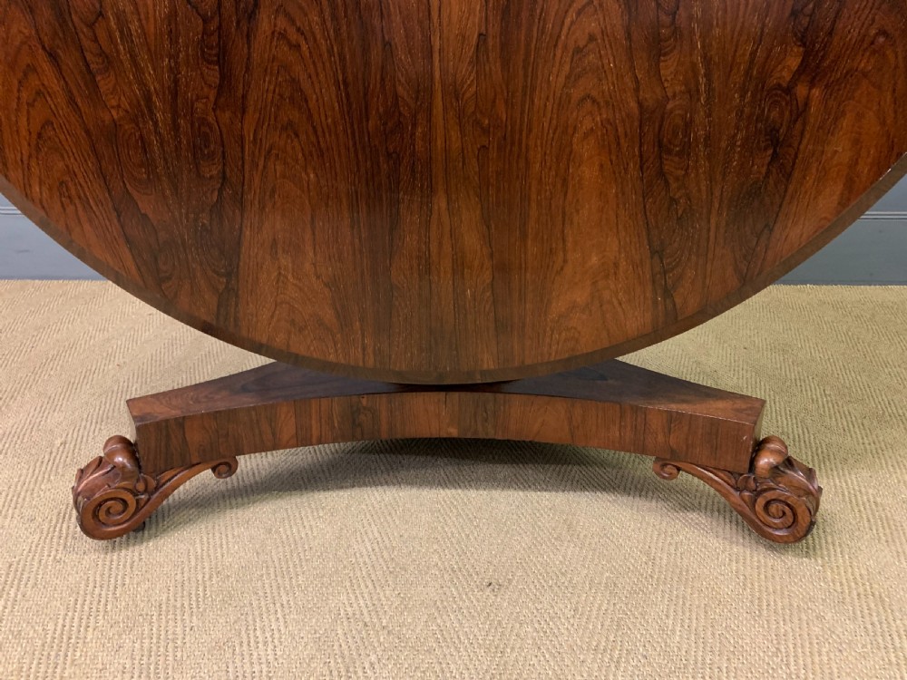 A William IV rosewood tilt-top loo table featuring a richly figured oval top mounted on a turned pedestal and a tri-form base with carved feet. View XIII