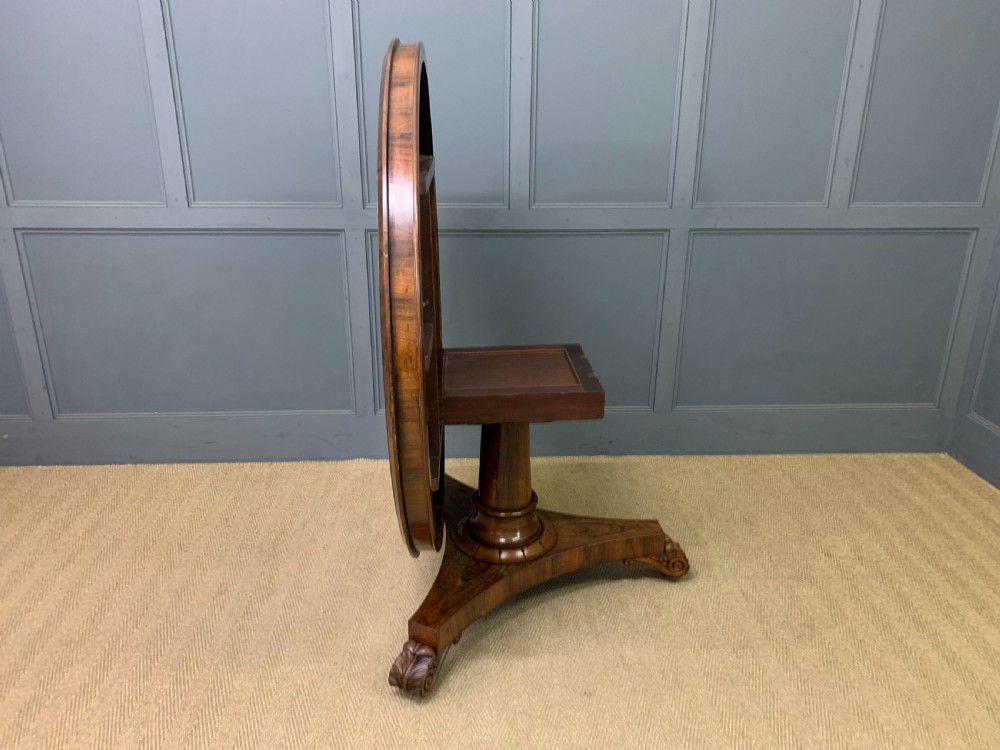 A William IV rosewood tilt-top loo table featuring a richly figured oval top mounted on a turned pedestal and a tri-form base with carved feet. View XIV