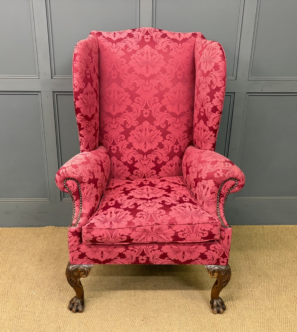 Late nineteenth-century wingback armchair upholstered in red damask fabric, featuring carved walnut cabriole legs with claw and ball feet.