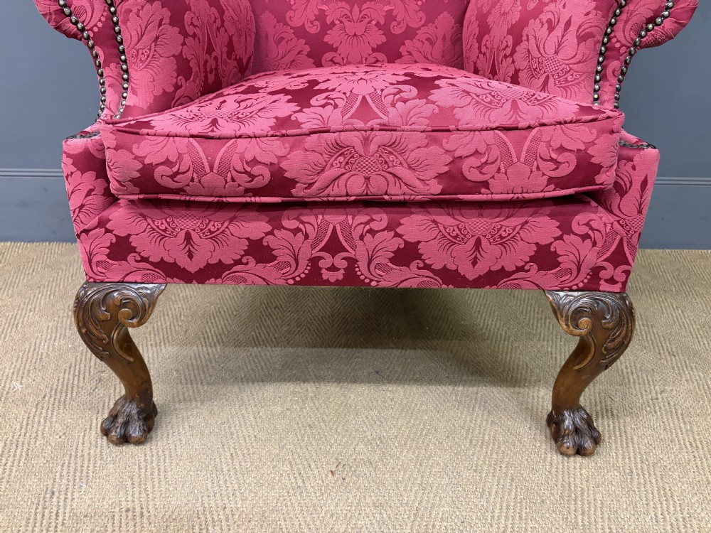 Late nineteenth-century wingback armchair upholstered in red damask fabric, featuring carved walnut cabriole legs with claw and ball feet. View V