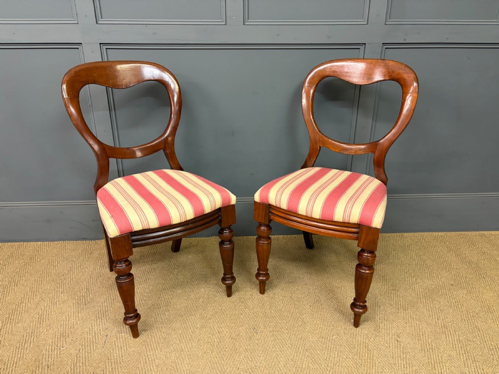 A set of ten Victorian mahogany balloon back dining chairs featuring turned front legs and red and cream striped upholstered seats. View VI
