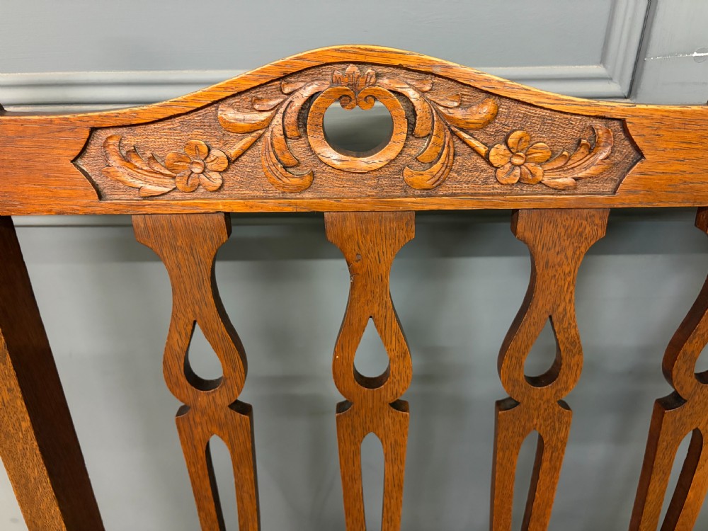 A five-piece Arts and Crafts oak salon suite comprising a two-seater settee, two armchairs, and two side chairs with carved crest rails and patterned upholstery. View VIII