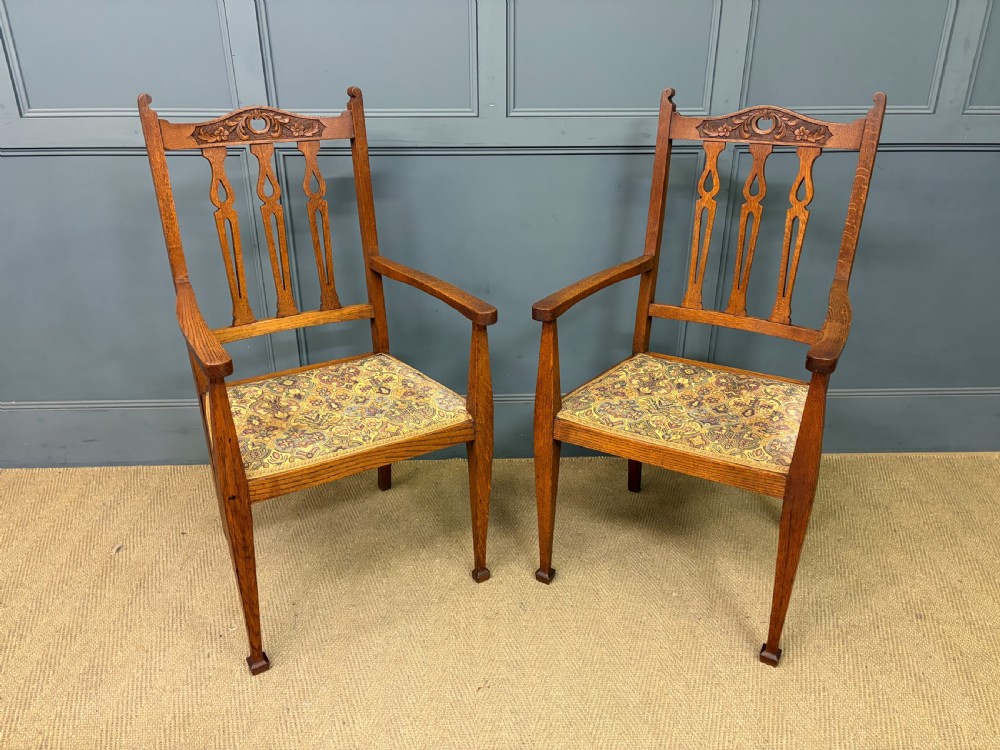 A five-piece Arts and Crafts oak salon suite comprising a two-seater settee, two armchairs, and two side chairs with carved crest rails and patterned upholstery. View XIV