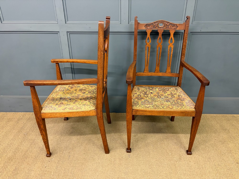 A five-piece Arts and Crafts oak salon suite comprising a two-seater settee, two armchairs, and two side chairs with carved crest rails and patterned upholstery. View XVI