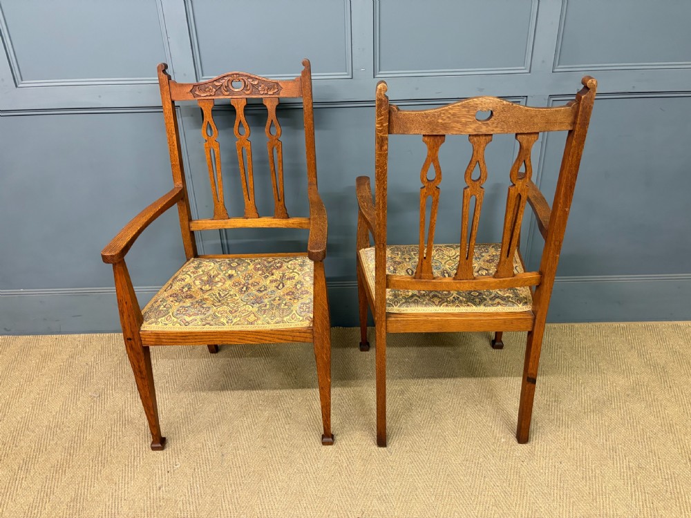 A five-piece Arts and Crafts oak salon suite comprising a two-seater settee, two armchairs, and two side chairs with carved crest rails and patterned upholstery. View XVII