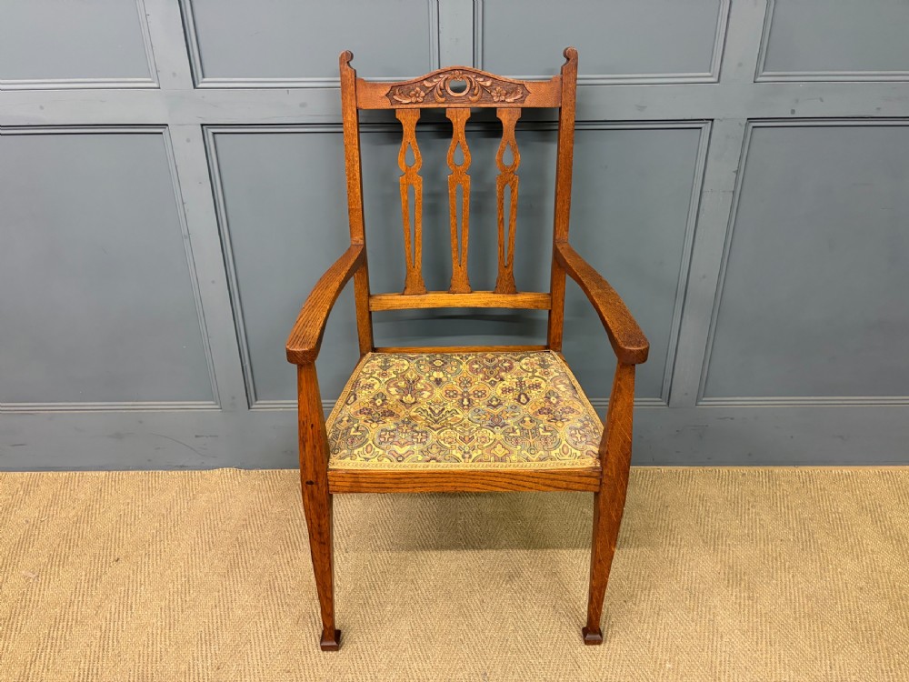 A five-piece Arts and Crafts oak salon suite comprising a two-seater settee, two armchairs, and two side chairs with carved crest rails and patterned upholstery. View XVIII