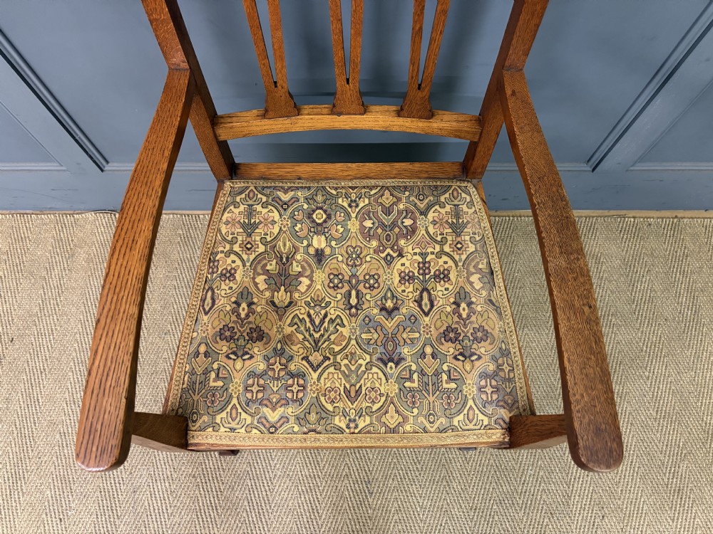 A five-piece Arts and Crafts oak salon suite comprising a two-seater settee, two armchairs, and two side chairs with carved crest rails and patterned upholstery. View XXI